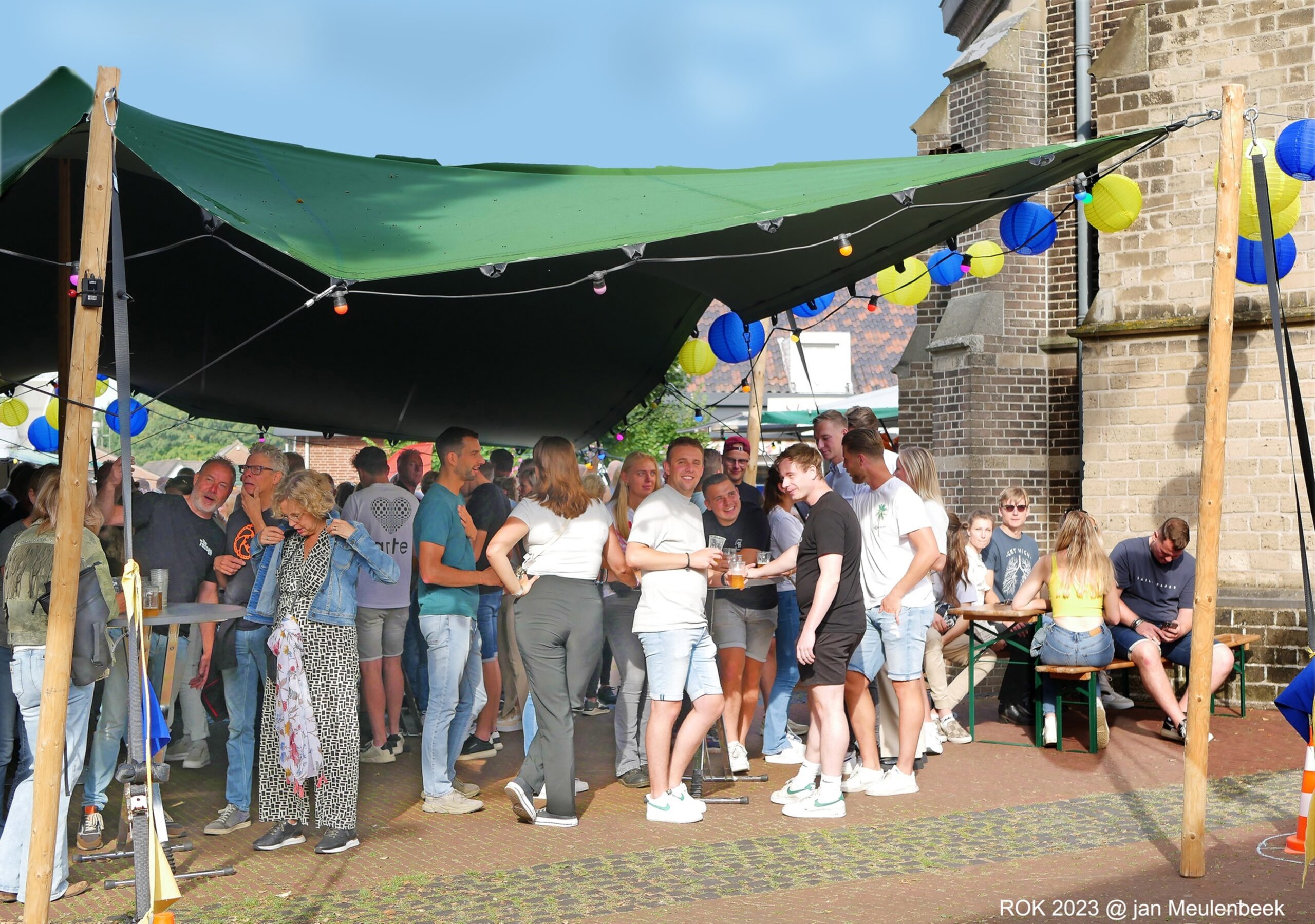 Bezoekers onder een groen zeil bij de kerk tijdens een feest in Wehl